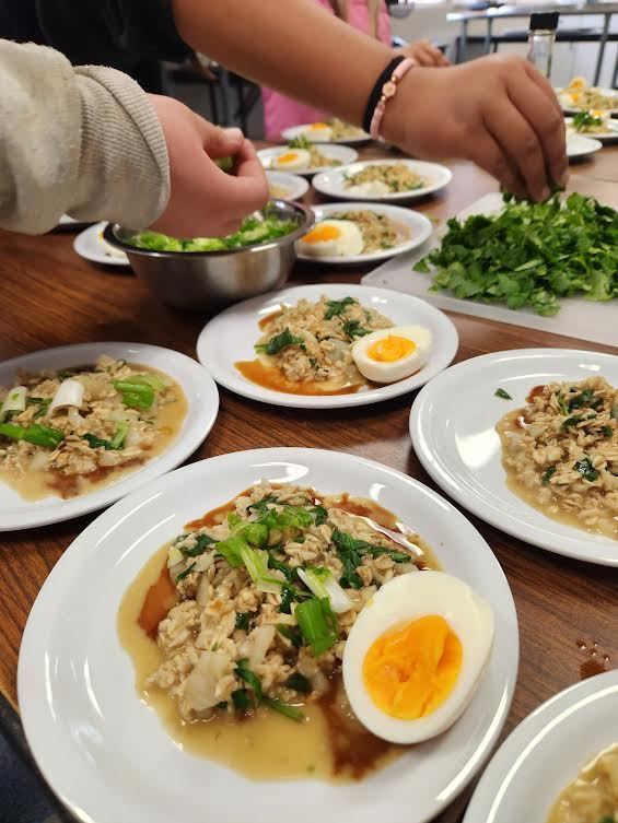 Two hands sprinkling herbs on plates of farm fresh food
