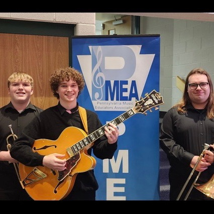 3 students standing by the PMEA banner