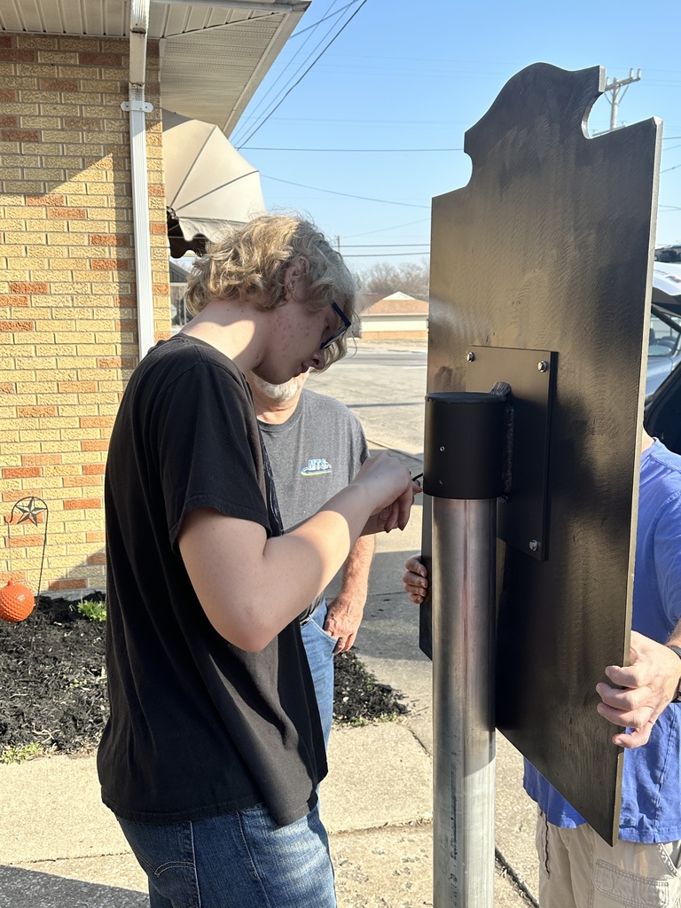 A student tightens the set screws to secure the sign to the post.