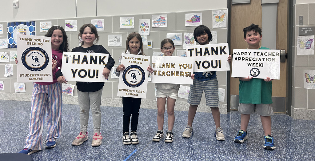 students smiling in a line holding signs that say thank yo u to teachers