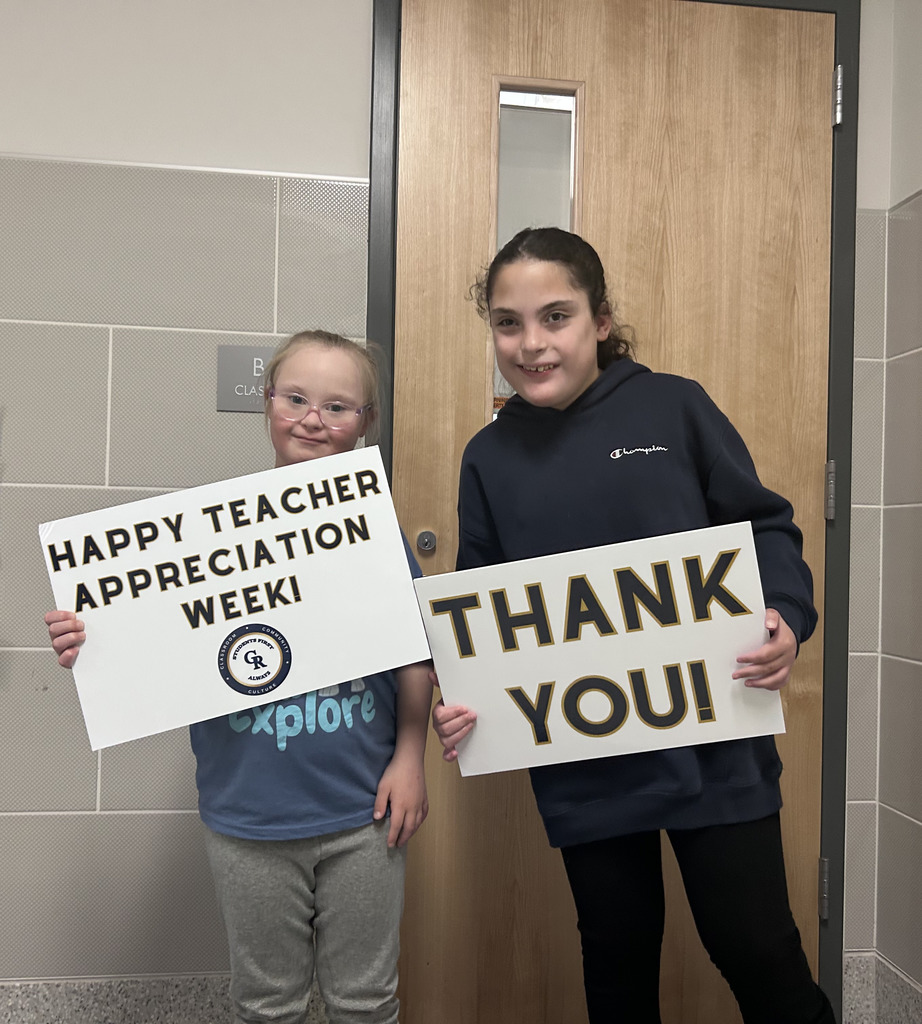two students smiling and holding signs that celebrate teacher appreciations