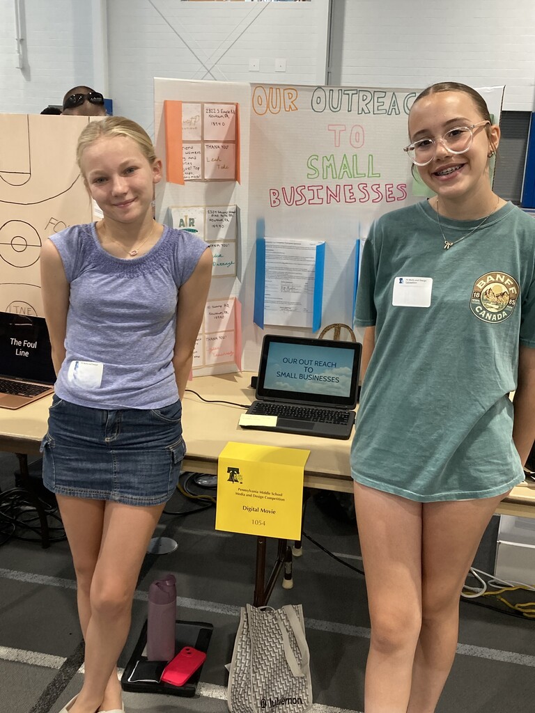 two students standing if front of their project for media contest