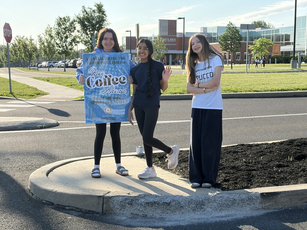 Students handing out coffee with a sign thanking parents