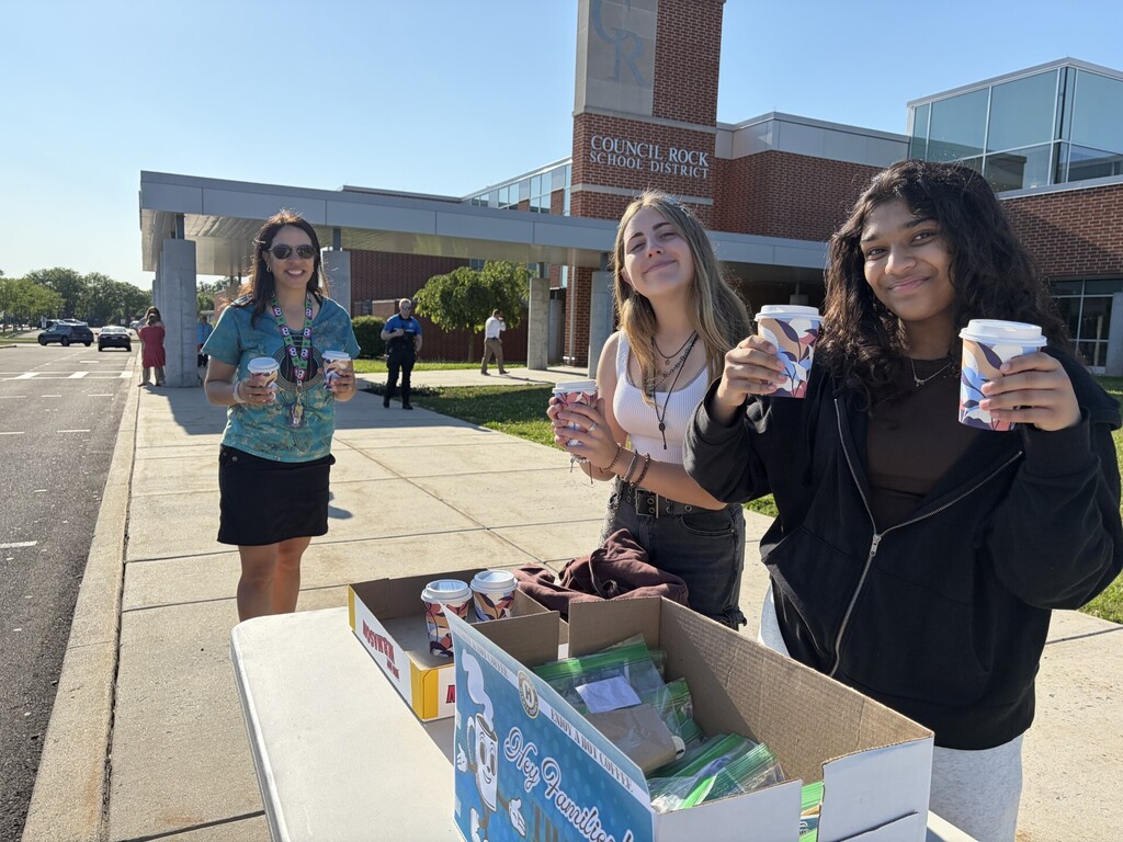 Students handing out coffee with a sign thanking parents