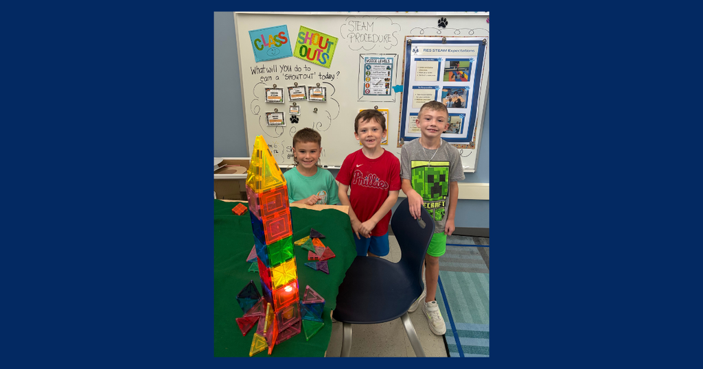 3 students standing in front of a magnitiles rocket that they built