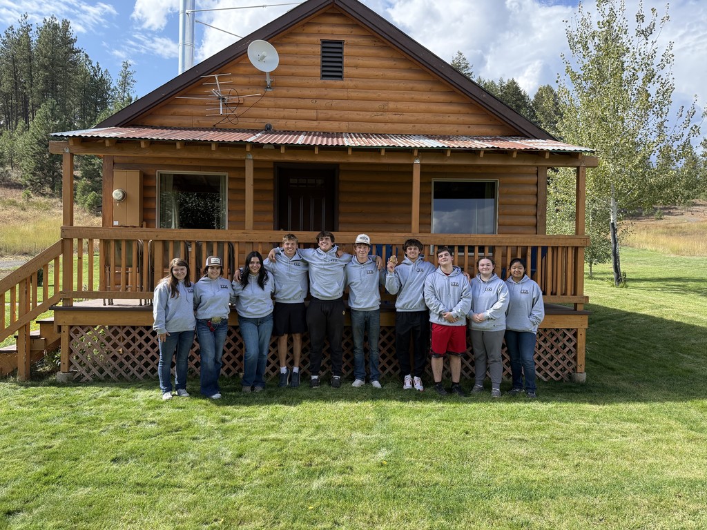 students in sweatshirts stand in front of a cabin