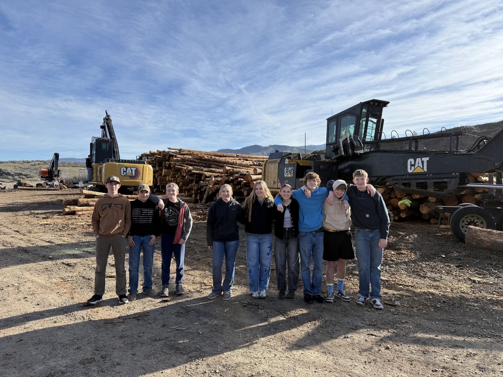students pose in front of logging equipment