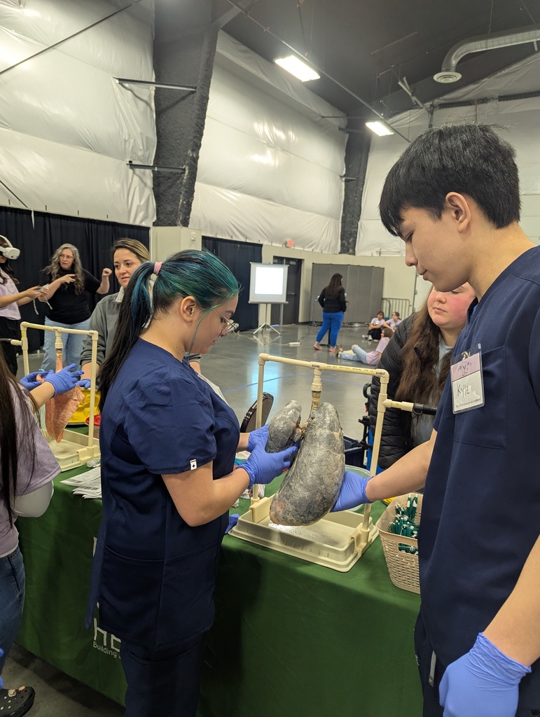 Several people examine a model in a large room. Two people in blue scrubs hold the model.