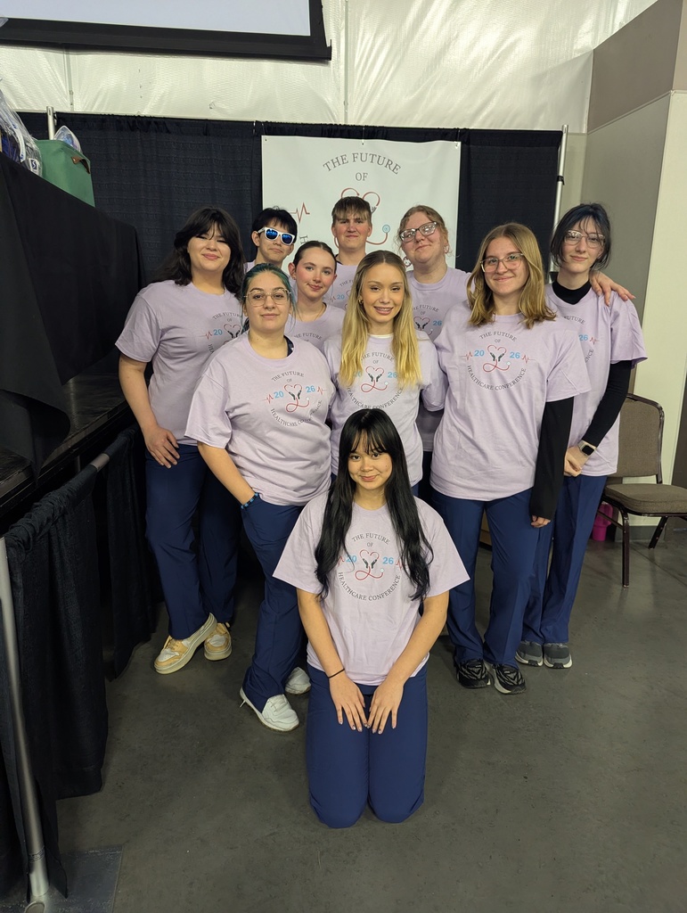 A group of individuals in matching light purple shirts and blue pants pose for a photo.