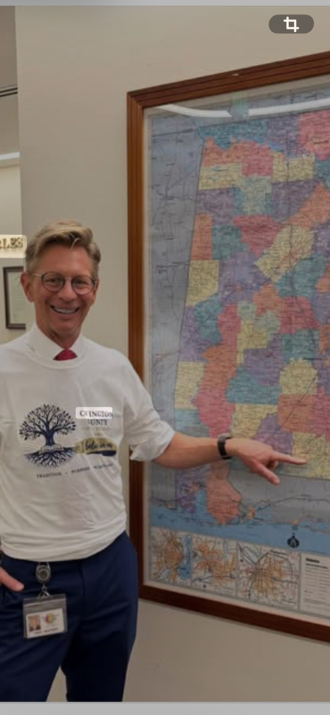 Dr. Eric Mackey, State Superintendent wearing a Covington County School tee shirt point to Covington County on the state map