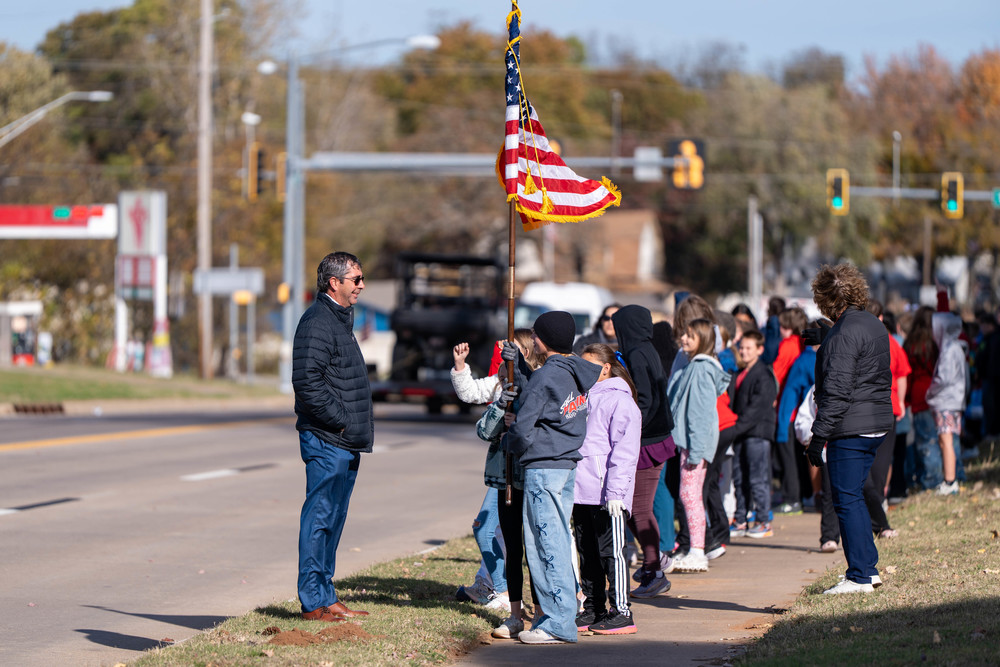 Kids and principal standing by a road with american flag