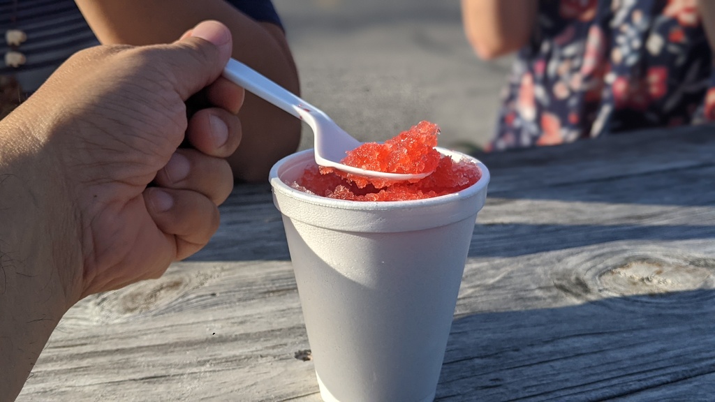 red sno cone in white cup on weathered wood picnic table