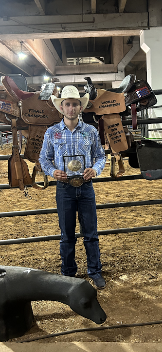 Male standing in a cowboy hat surrounded by prizes and holding a belt buckle