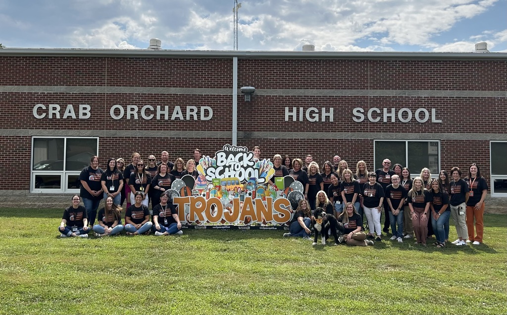 School staff wearing black and orange t-shirts standing in front of Crab Orchard High School