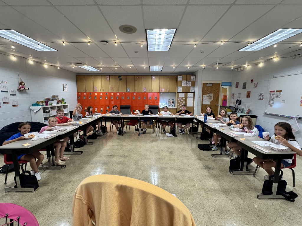 students seated at their desks in a horseshoe shape eating doughnuts