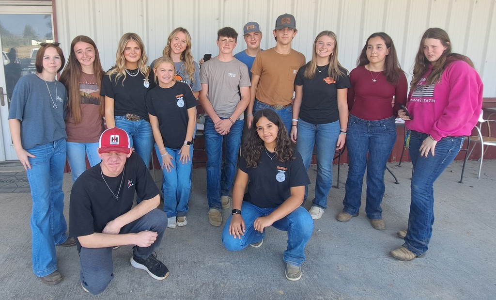 Group of 13 High School Students standing and kneeling in front of a tan & red building