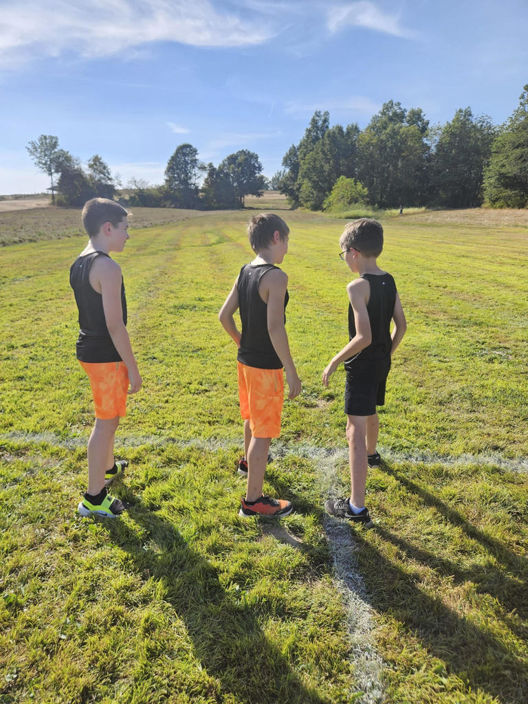 3 junior high cross country boys waiting to start the race wearing black and orange