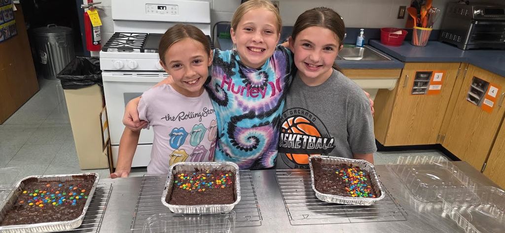 3 girls standing in front of 3 trays of brownies