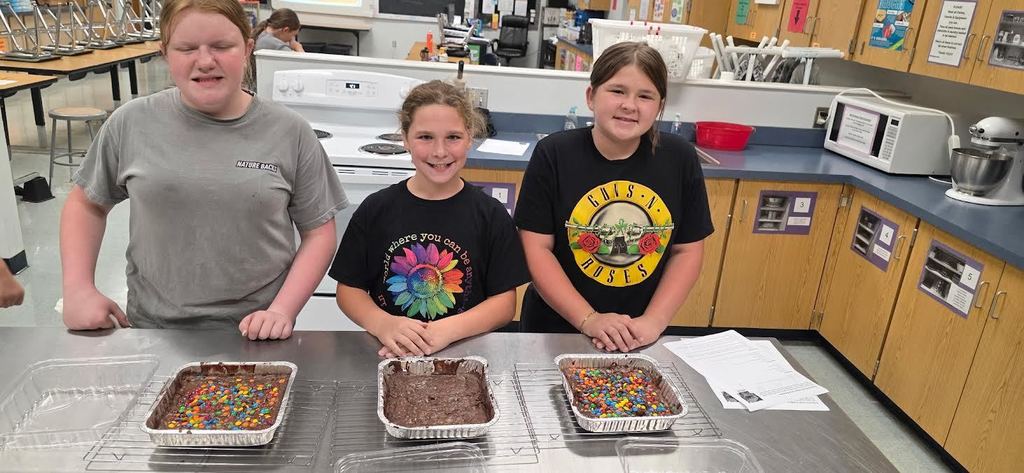 3 girls standing in front of 3 trays of brownies