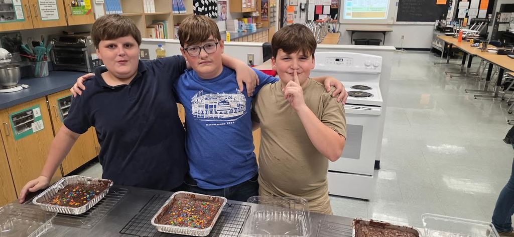 3 boys standing in front of 3 trays of brownies