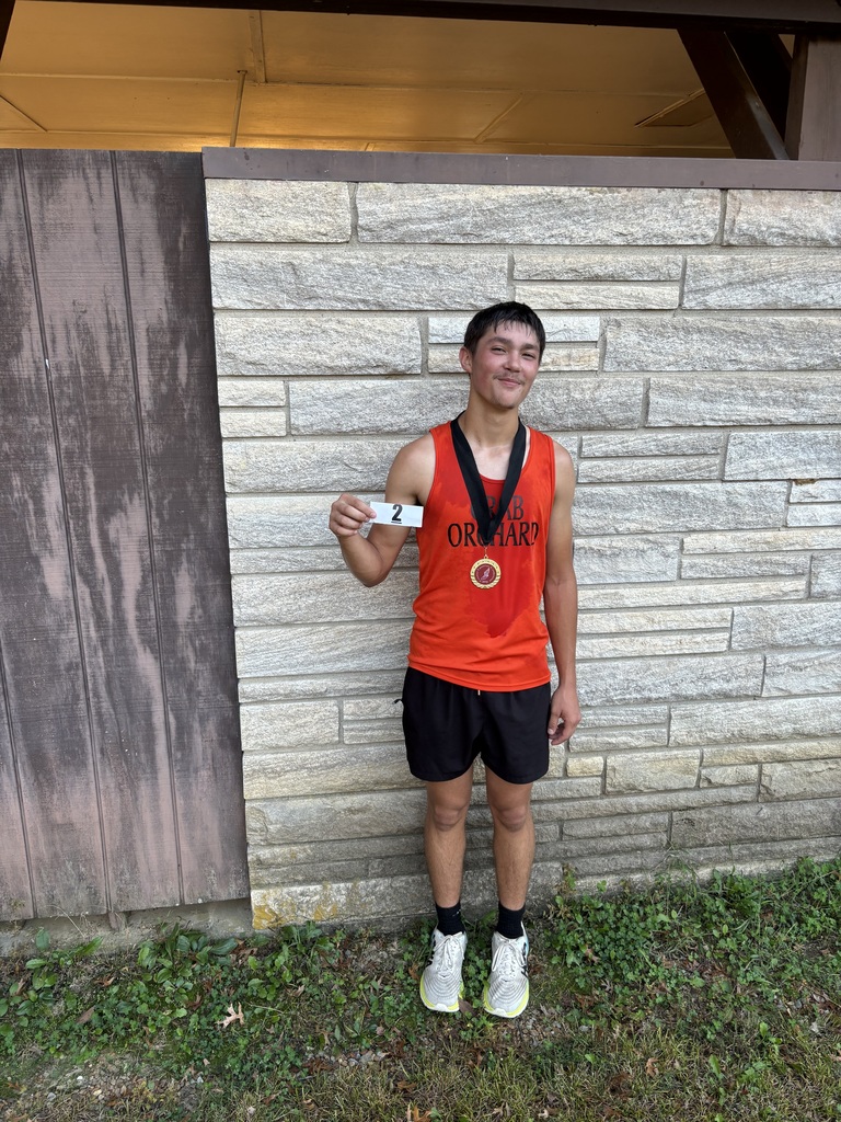Athlete standing holding ribbon and wearing a medal. Orange jersey and black pants