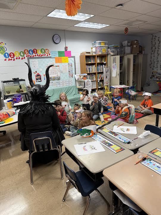 kindergarten class sitting on the floor listening to a mystery reader dressed as Maleficent