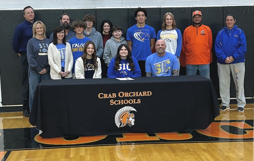 Group of people standing and sitting with student signing scholarships 