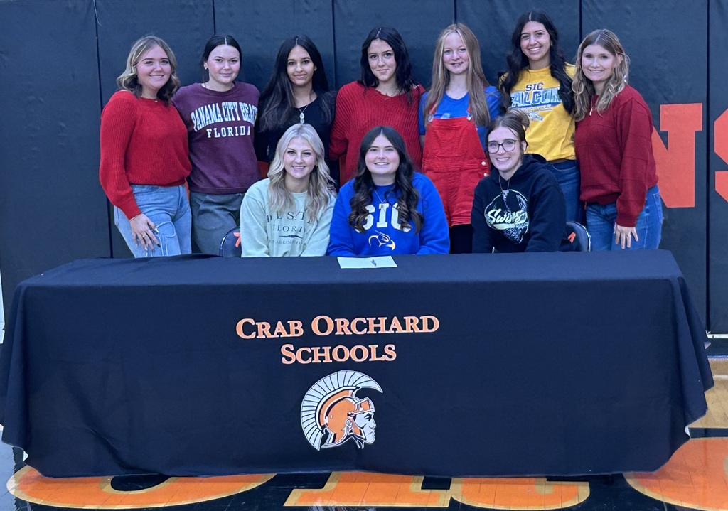 Group of girls sitting with softball player signing her scholarship 
