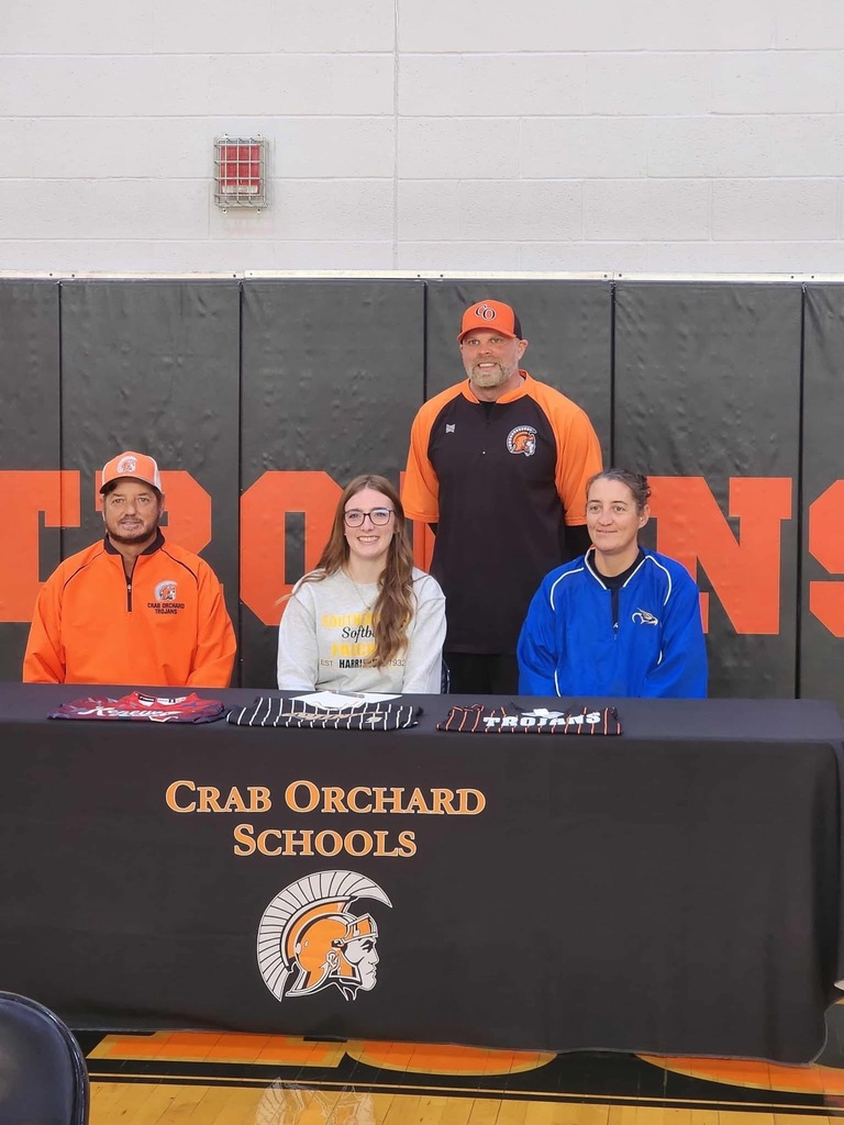 Coaches and a player sitting center behind a black table for a signing 