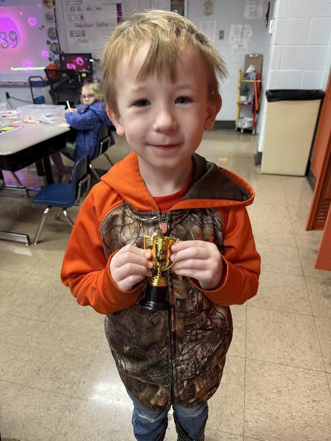 kindergartener with blonde hair holding a small trophy