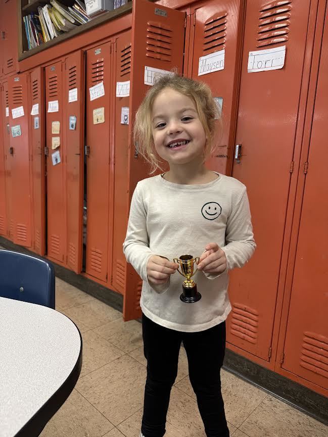 kindergartener with blonde hair holding a small trophy