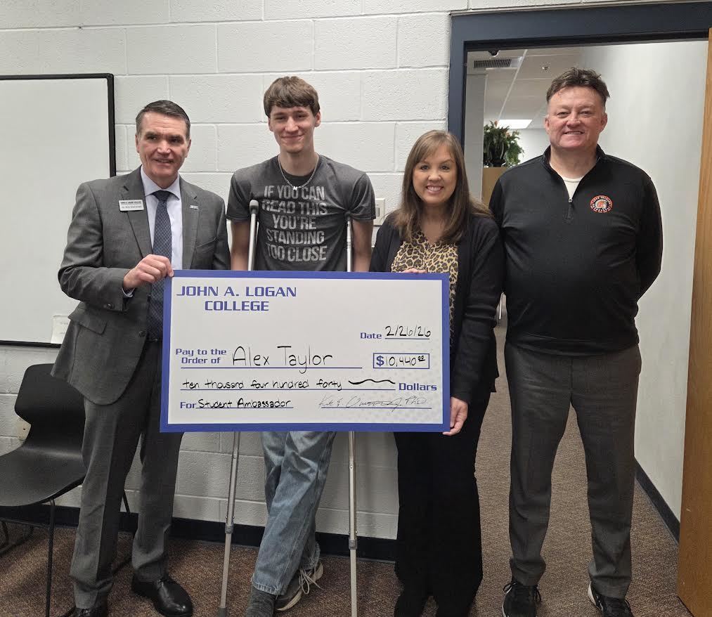 High school senior on crutches, standing with three adults,  receiving a large check for a college scholarship