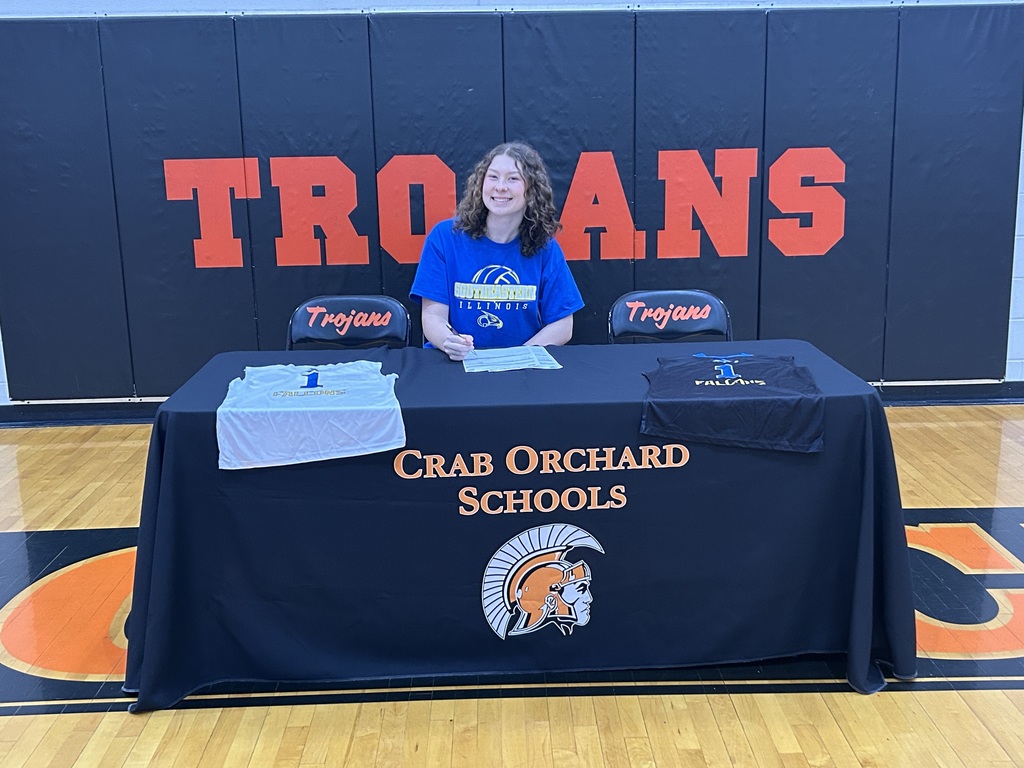 Player in blue shirts sitting behind being black table signing paper