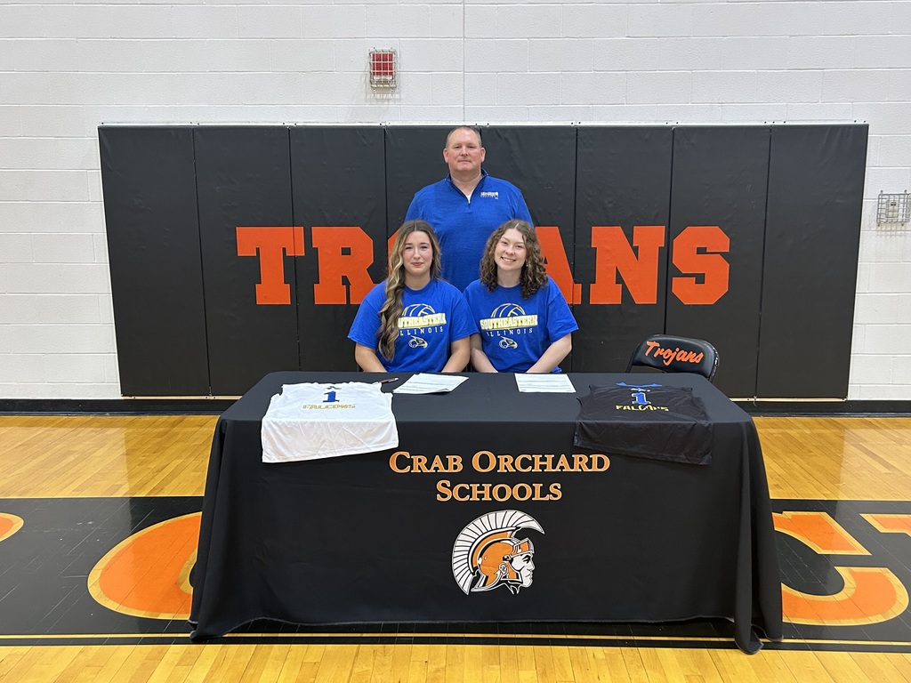 Players in blue shirts with coach behind them in blueshirts sitting behind black table 