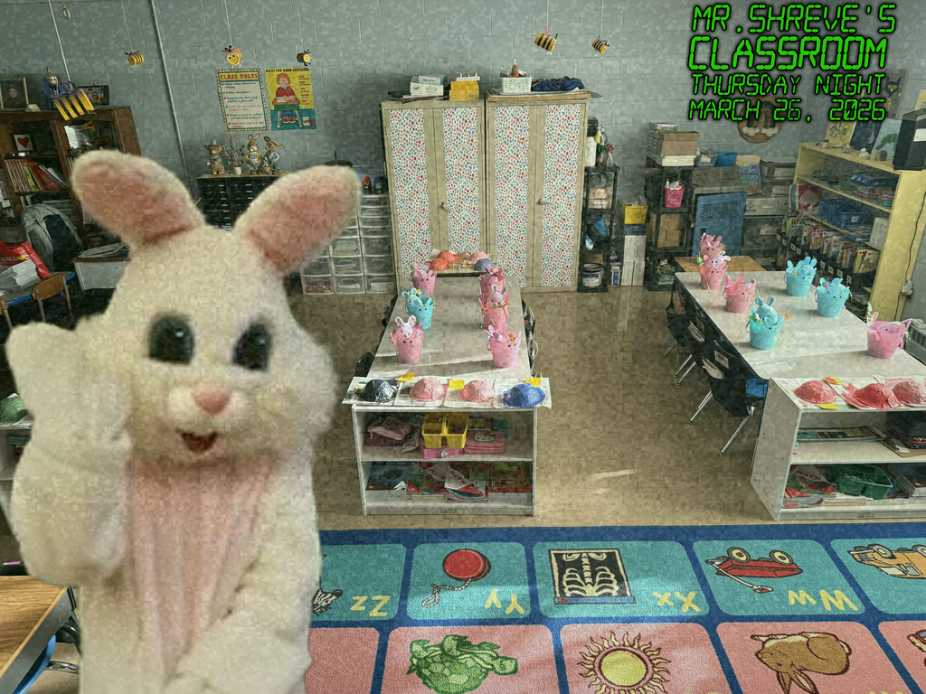 the easter bunny waving standing in front of two tables in a first grade classroom