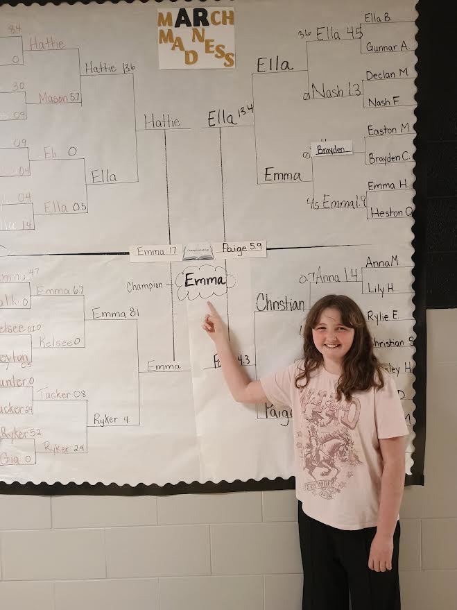 4th grade female student wearing a light pink shirt standing in front of a hand written AR reading bracket