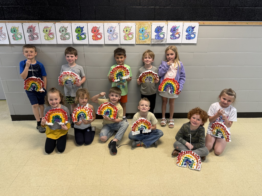 elementary students sitting and standing in hallway holding rainbows
