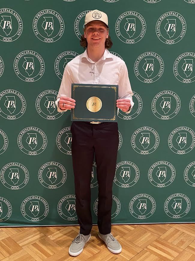 high school  male student holding a certificate standing in front of a green IPA sign