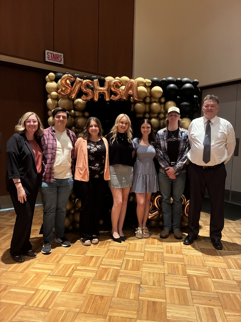 5 high school students (3 females and 2 males) standing with two adults (1 male and 1 female) standing in front of black and gold balloons 