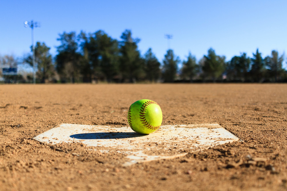 a yellow softball with red stitching sitting on home plate