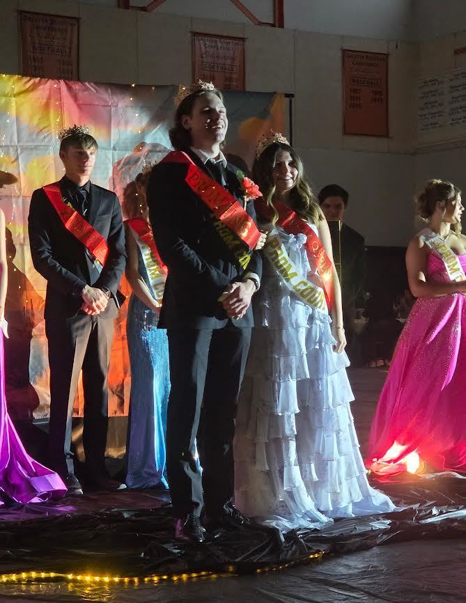 prom king and prom queen standing next to each other wearing a red sash