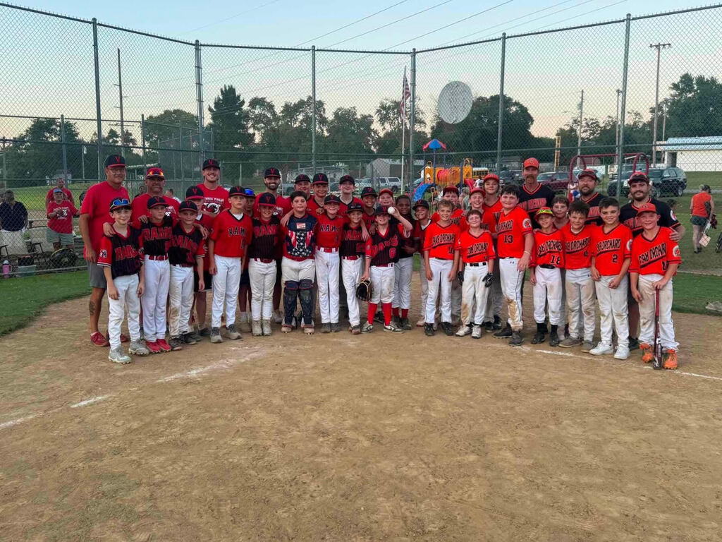 Two junior high boys baseball teams standing together on a baseball infield, wearing black, orange and white