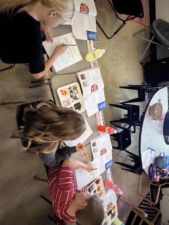 3 5th grade students working at their desks with candy on trays, drinks, notebooks and workshseets