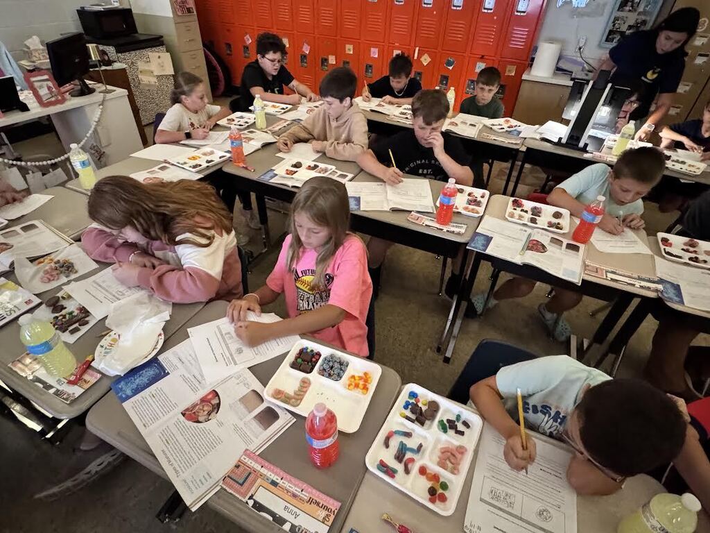 5th grade class sitting at desks with candy on trays, notebooks and worksheets
