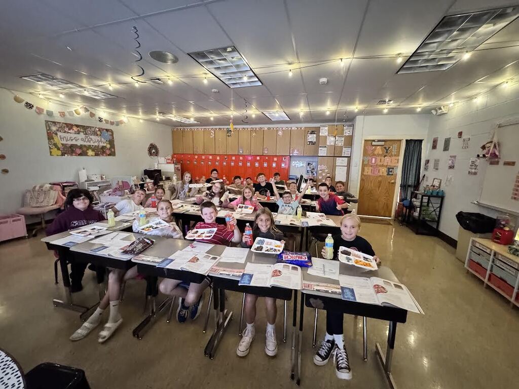 5th grade class sitting at desks with candy on trays and drinks
