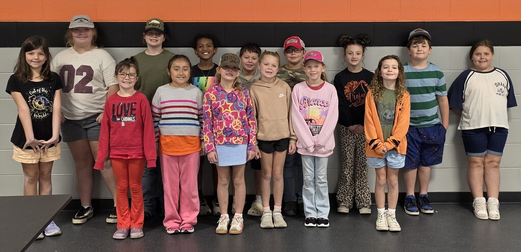 elementary students standing against a gray wall with black & orange stripes above their head