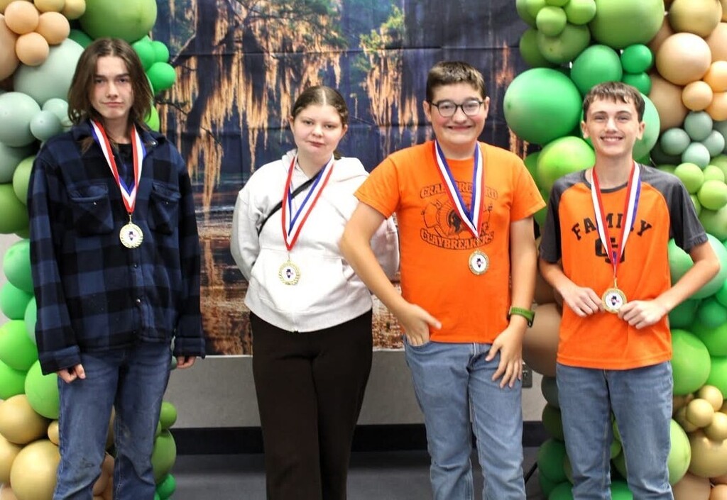 8th Grade students with medals standing in front of green & gold balloons and a swamp backdrop