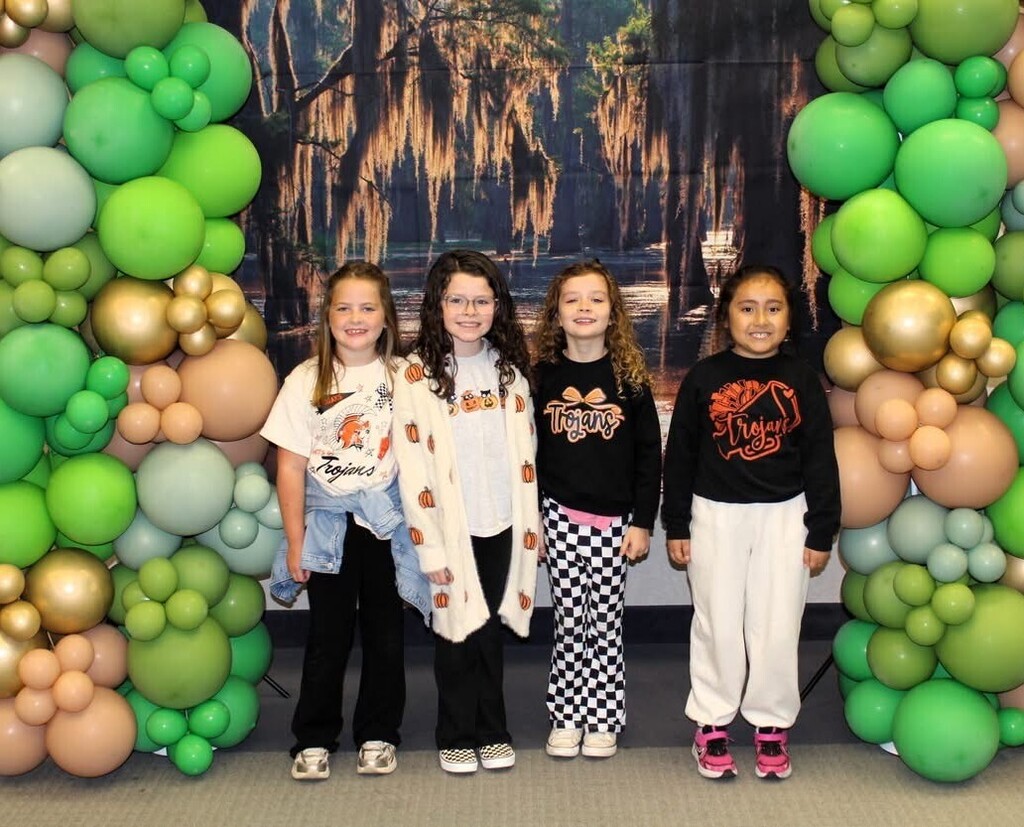 3rd grade girls standing in front of green and gold balloons and a swamp backdrop