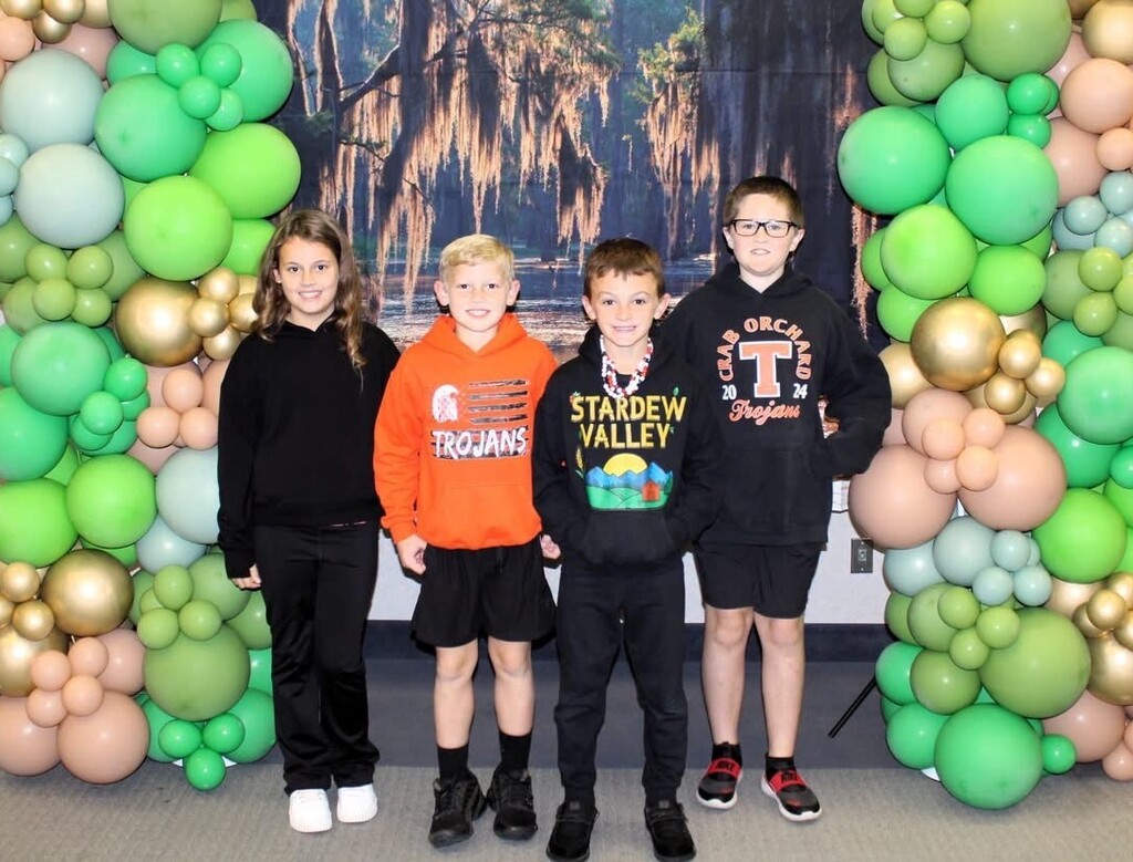 4th grade students standing in front of green & gold balloons and a swamp backdrop
