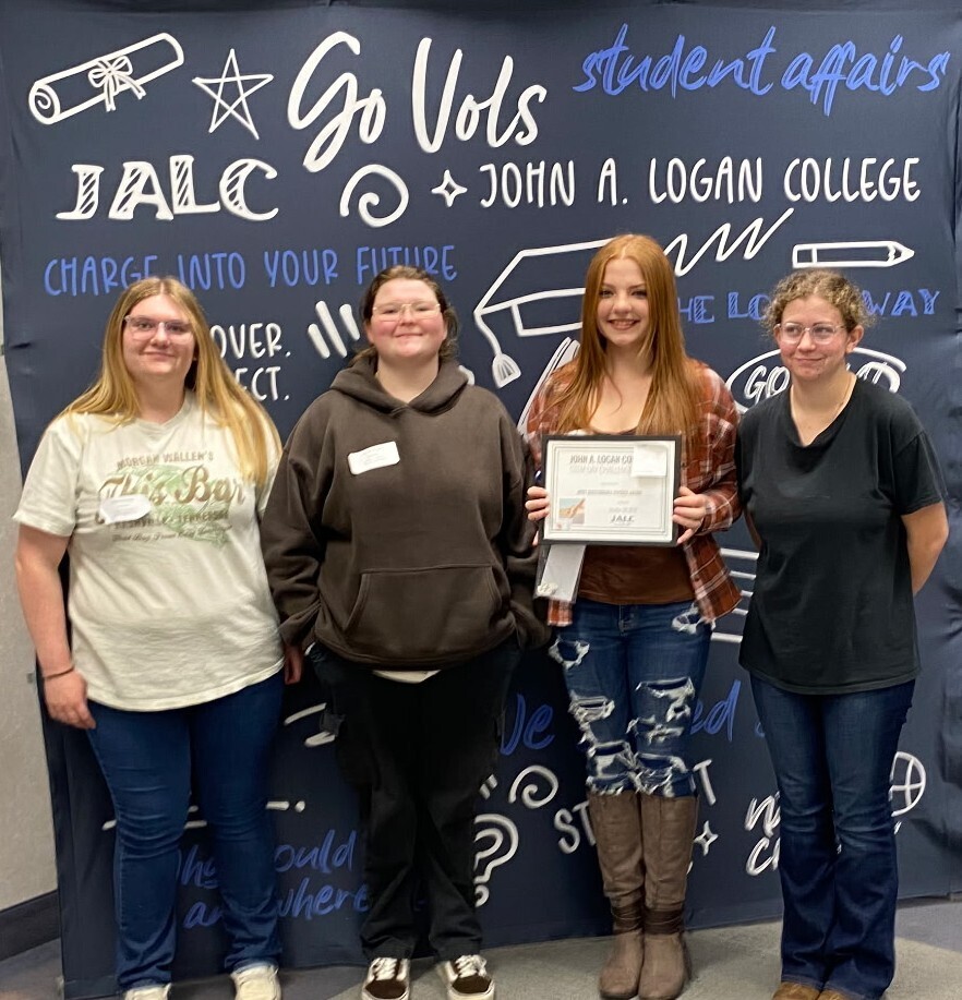 4 young ladies holding a certificate in front of a John A Logan College banner